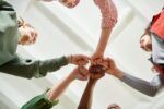 The camera looks up on five people in circle formation putting their fists together